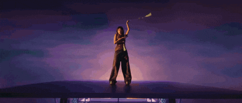a woman in a black jumpsuit is standing on a stage holding a sword .