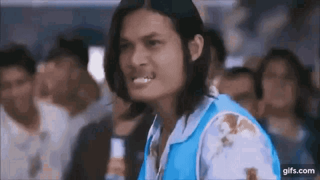 a man with long hair is making a funny face in front of a crowd .