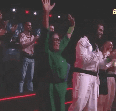 a woman in a green shirt is raising her hands in the air while a group of people applaud .