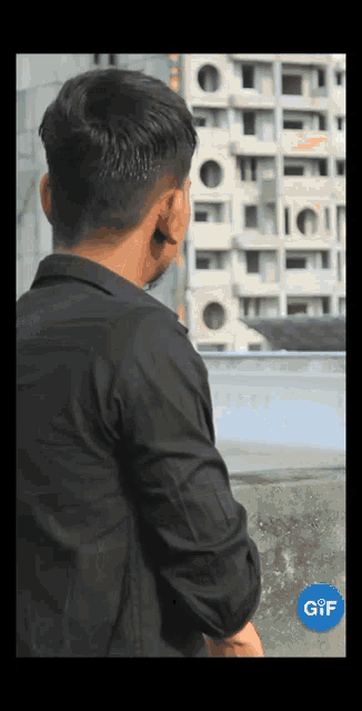 a man in a black shirt is standing in front of a building with a gif logo on the bottom left