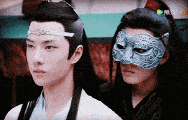 a man wearing a mask stands next to another man in a white shirt