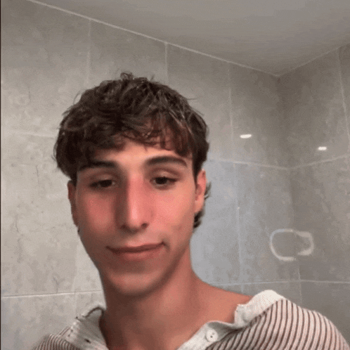 a young man in a striped shirt is smiling in front of a wall with a c on it
