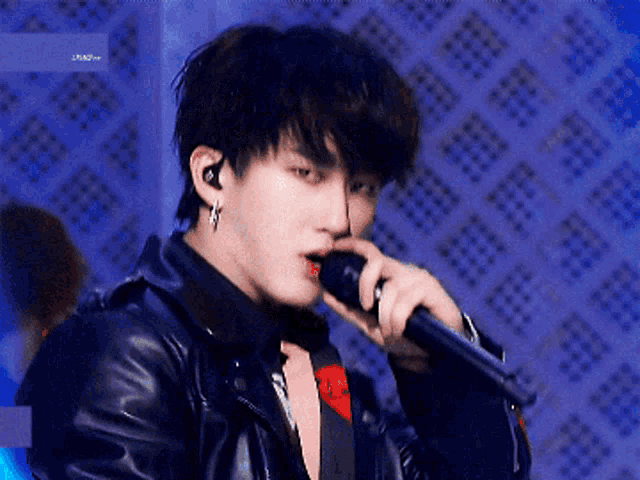 a young man is singing into a microphone while wearing a leather jacket and earrings .
