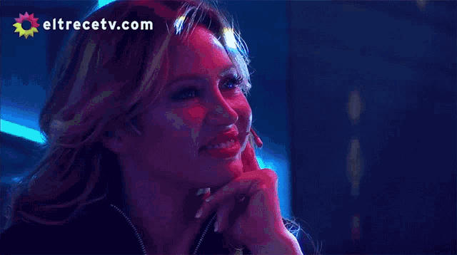 a woman is smiling in front of a screen that says eltrecetv.com on it