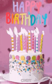 a birthday cake with candles and sprinkles on a pink table .