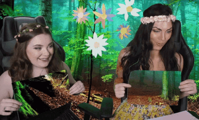 two women are sitting in chairs in front of a forest with flowers