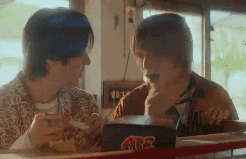two young men are sitting at a table in a diner eating hamburgers .