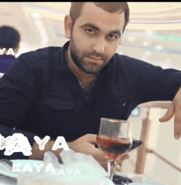 a man sitting at a table with a glass of wine and the word kaya on the bottom left