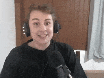 a young man wearing headphones is sitting in front of a microphone and smiling .