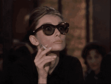 a woman wearing sunglasses holds a cigarette in her hand