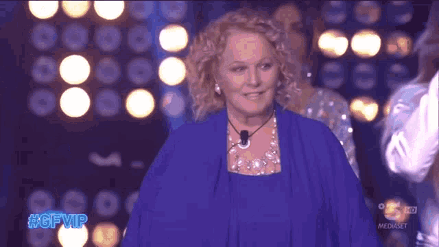 a woman in a blue dress stands on a stage with the hashtag #gfvip on the bottom