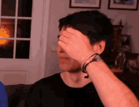 a man is covering his face with his hand while wearing headphones .