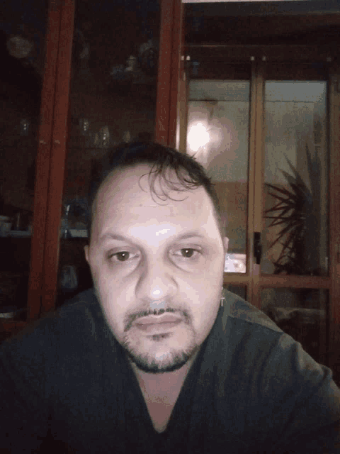 a man with a beard looks at the camera in front of a glass door