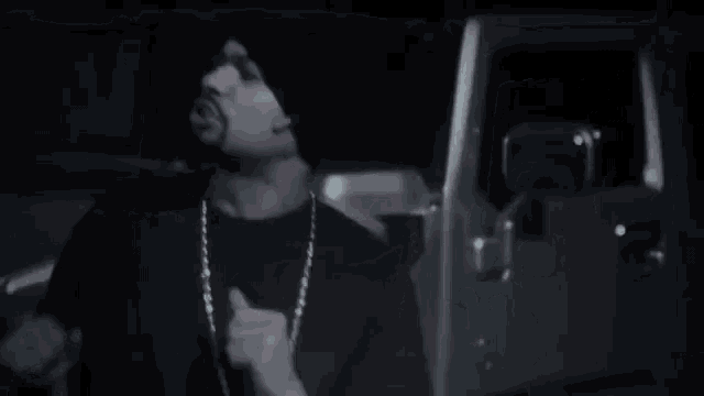 a man wearing a beanie and a necklace is standing in front of a car