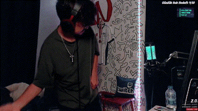 a man wearing headphones is standing in front of a wall that has a pillow that says twitch on it