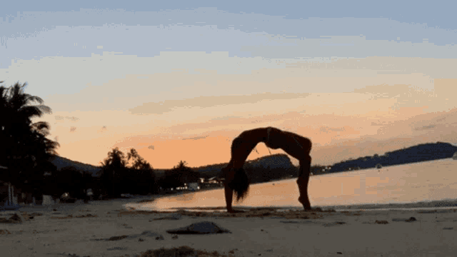 a woman does a yoga pose on the beach at sunset
