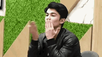 a young man in a black leather jacket is blowing a kiss .