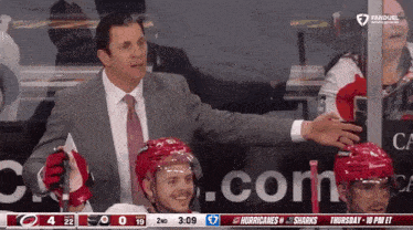 a man in a suit and tie talks to a hockey player