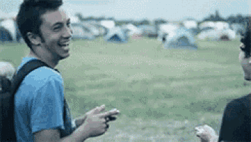 two men are standing in a field with tents in the background and laughing .