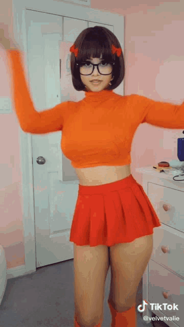 a woman in a velma scooby doo costume is dancing in a pink room .