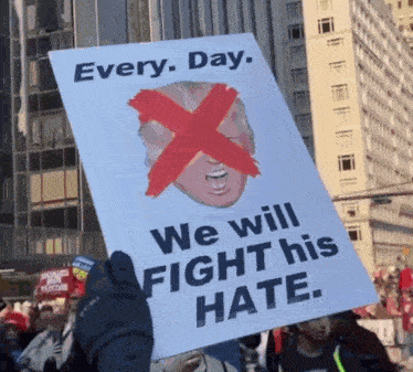 a protester holds up a sign that says every day we will fight his hate