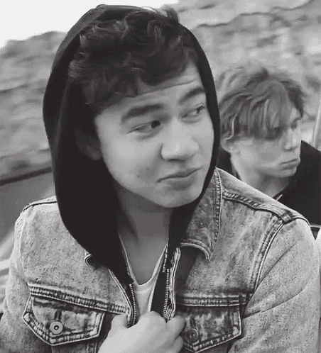 a black and white photo of a young man wearing a denim jacket and a hoodie .