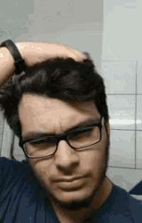 a man wearing glasses and a blue shirt is scratching his hair .