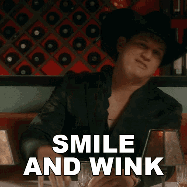 a man sitting at a table with a glass of whiskey and the words smile and wink above him