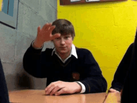 a boy in a school uniform is sitting at a desk and making a funny face .