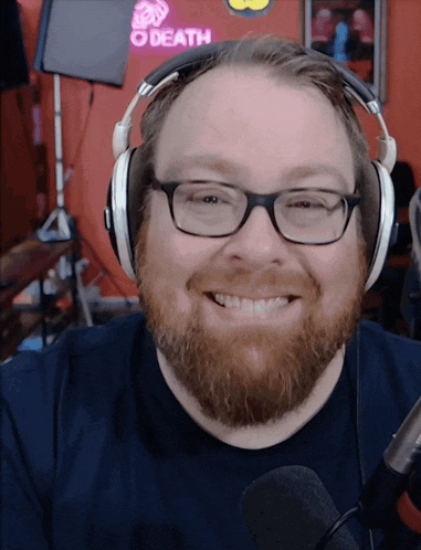 a man wearing glasses and headphones is smiling in front of a neon sign that says death