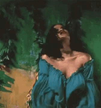 a woman in a blue off the shoulder dress is laying on a green surface .