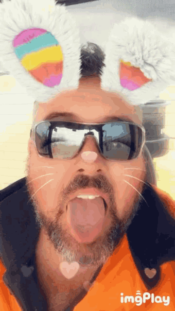 a man wearing sunglasses and bunny ears shows his tongue