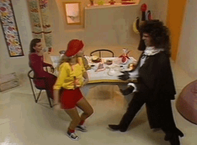 a woman in a yellow shirt is dancing with a man in a black suit in front of a table