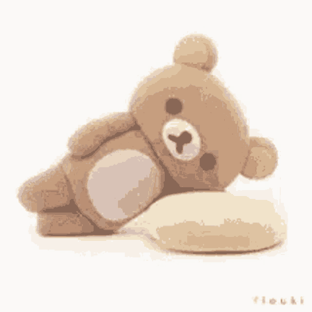 a teddy bear is laying down on a pillow .