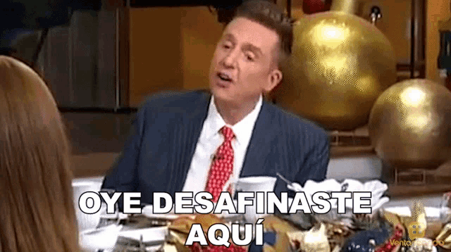 a man in a suit and tie is sitting at a table with a woman and says oye desafinaste aqui .