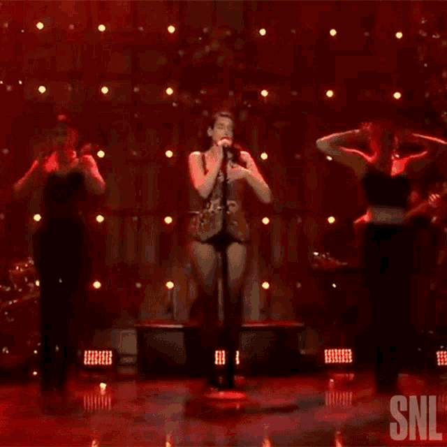a woman is singing into a microphone on a stage with a snl logo behind her .