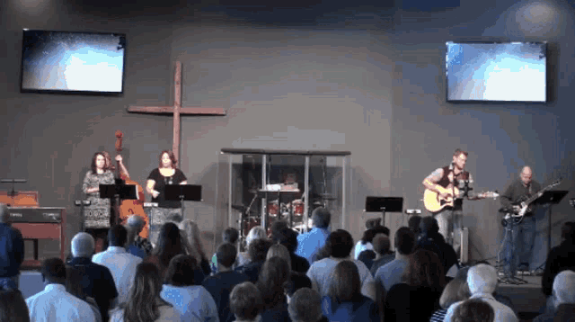 a group of people are sitting in front of a stage with a cross in the background