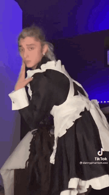 a man in a maid costume is dancing in a room with a blue light behind him .