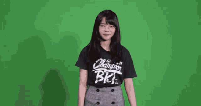 a girl wearing a black champion bk t-shirt stands in front of a green screen