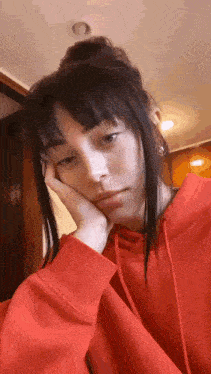 a woman wearing a red hoodie is holding her head with her hand .