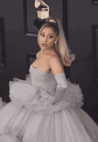 a woman in a white dress and white gloves stands in front of a grammy statue