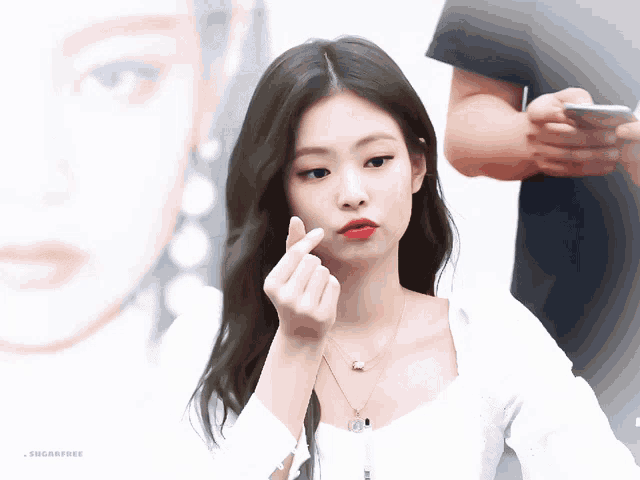 a woman making a heart shape with her finger while wearing a white top