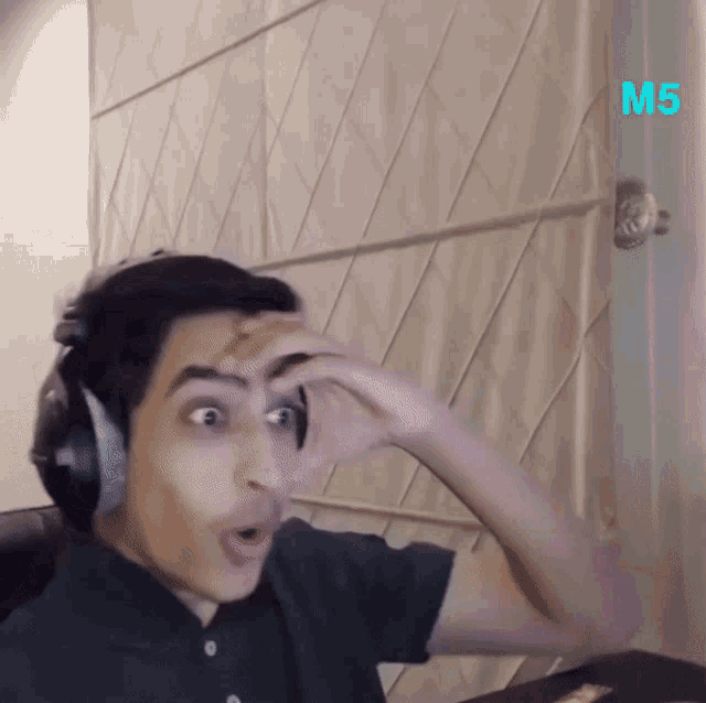 a man wearing headphones is making a funny face in front of a door that has the letter m on it