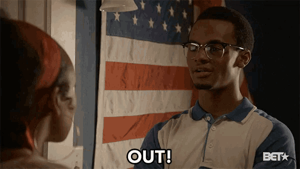 a man wearing glasses says out in front of a flag