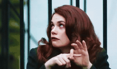 a woman with red hair is making a gesture with her hands while looking up .