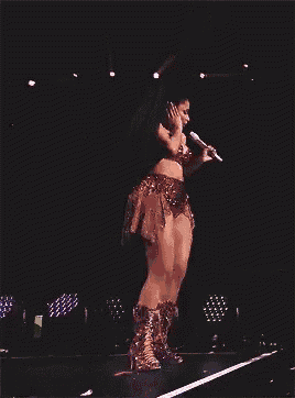 a woman is singing into a microphone on a stage in a dark room