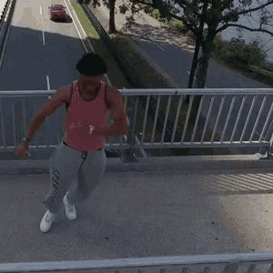 a man in a pink tank top and gray sweatpants is dancing on a bridge
