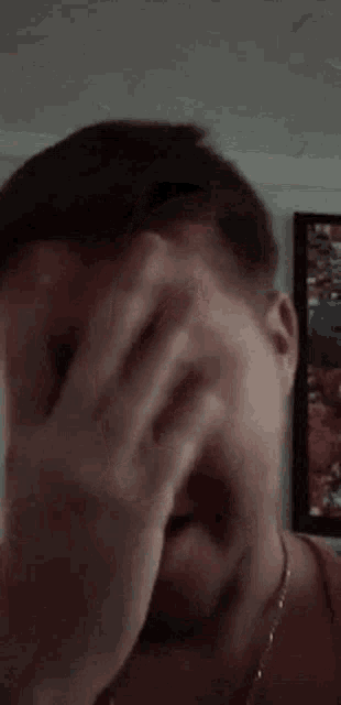 a man with a beard is covering his face with his hands .