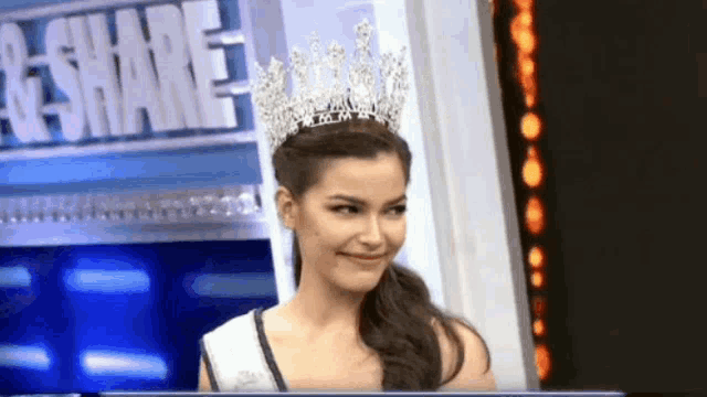 a woman wearing a crown stands in front of a sign that says " share "