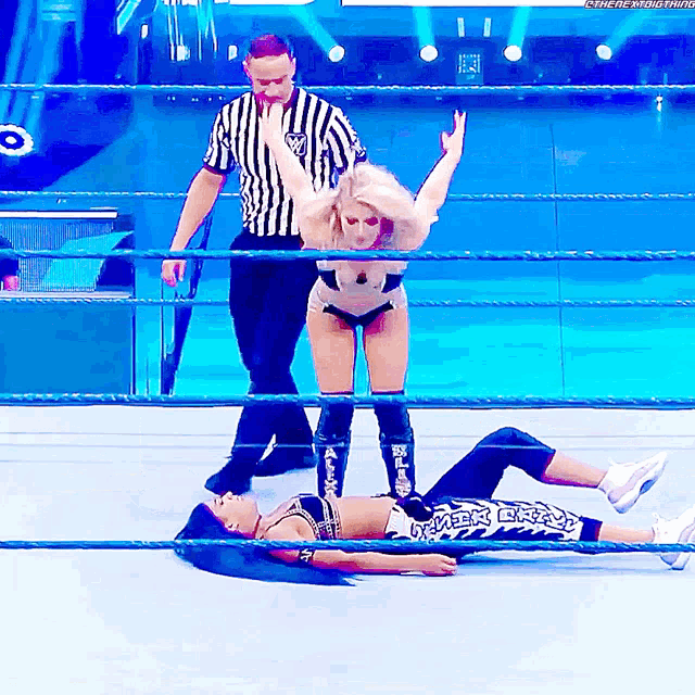 a female wrestler is laying on the ground in a wrestling ring while a referee looks on